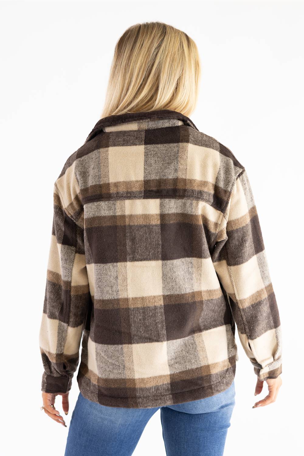 A woman viewed from the back wearing a brown, beige, and gray buffalo plaid flannel shirt jacket with blue jeans, set against a plain white background.