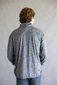 A man viewed from behind wearing a gray long-sleeve button-up shirt with a lighter gray abstract organic pattern, paired with blue jeans, against a plain gray studio background.