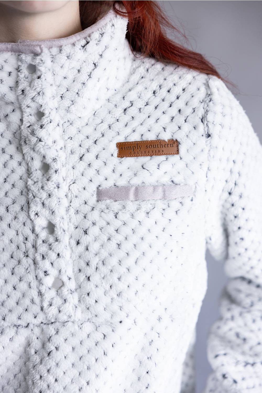 Close-up of a person wearing a white textured knit top with a small brown leather patch reading simply southern on the chest.