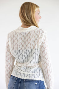 A woman shown from the back wearing a cream lace long-sleeve wrap top and blue jeans against a plain white background.