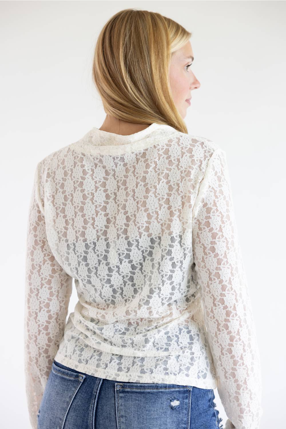 A woman shown from the back wearing a cream lace long-sleeve wrap top and blue jeans against a plain white background.