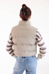 A person shown from the back wearing a light beige puffer vest over a purple and cream striped knit sweater, paired with light blue jeans, against a plain white background.