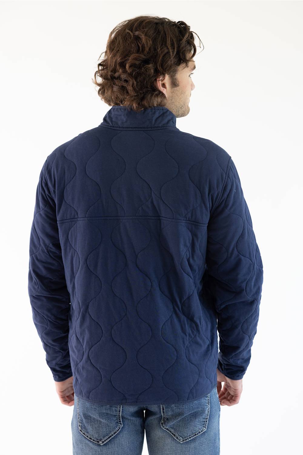 A man wearing a navy blue Patagonia quilted pullover jacket with a stand collar and zippered chest pocket, paired with blue jeans, against a plain white studio background.