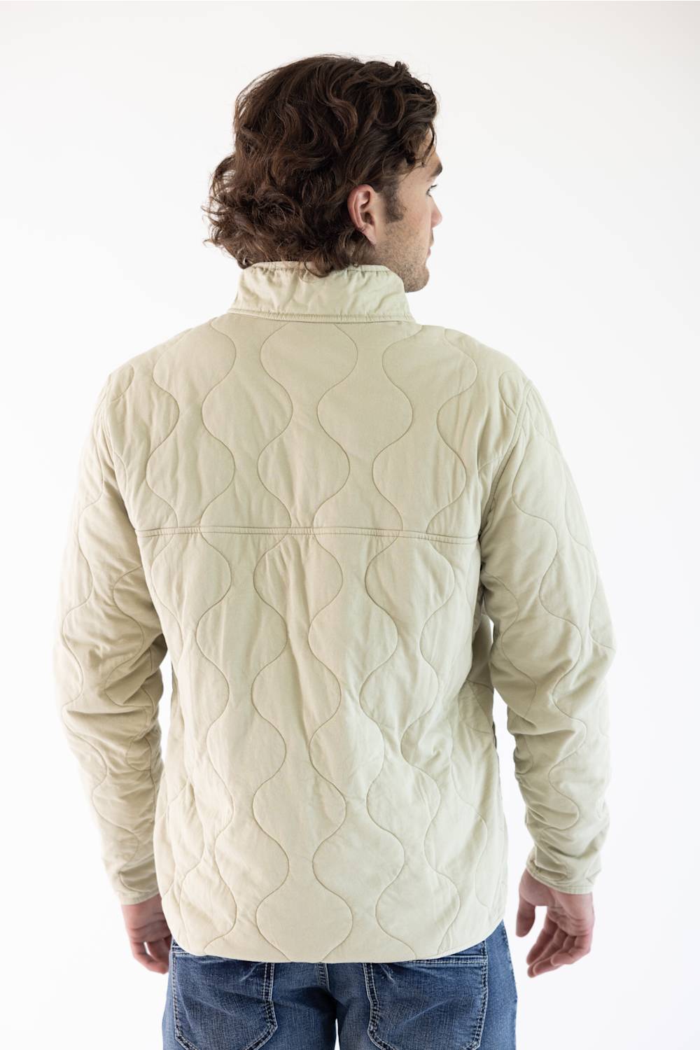 A man viewed from the back wearing an off white Patagonia quilted pullover jacket with a stand collar and zippered chest pocket, paired with blue jeans, against a plain white studio background.