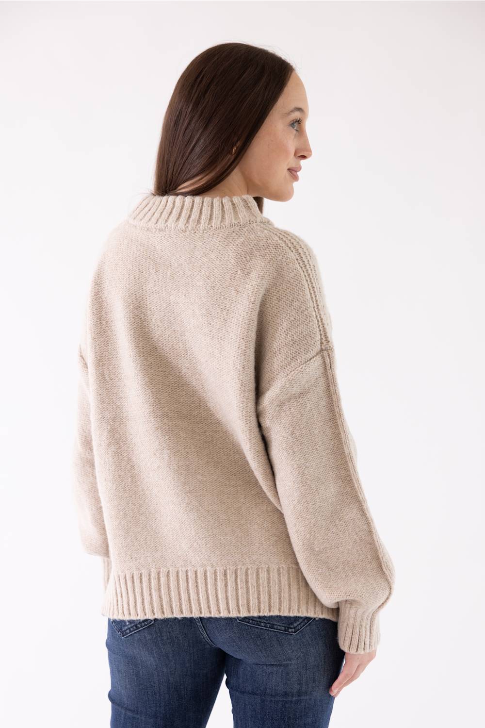 A woman modeling the Pink Rose Mock Neck Sweater in Heather Oatmeal, featuring a ribbed mock neck, drop shoulders, and long sleeves with ribbed cuffs, paired with dark-wash jeans.