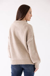 A woman modeling the Pink Rose Mock Neck Sweater in Heather Oatmeal, featuring a ribbed mock neck, drop shoulders, and long sleeves with ribbed cuffs, paired with dark-wash jeans.