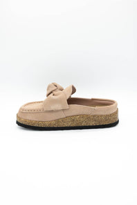 A single slip-on mule shoe in blush suede with a matching fabric bow on the vamp and a cork-textured midsole, shown against a plain white background.