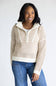 A woman wearing a cream and tan open-knit half-zip pullover sweater with a mock neck, paired with blue jeans, against a plain light gray background.