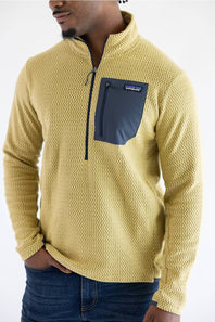 A man wearing a yellow textured quarter-zip fleece pullover with a dark navy chest pocket and zipper, paired with blue jeans, against a plain white background.