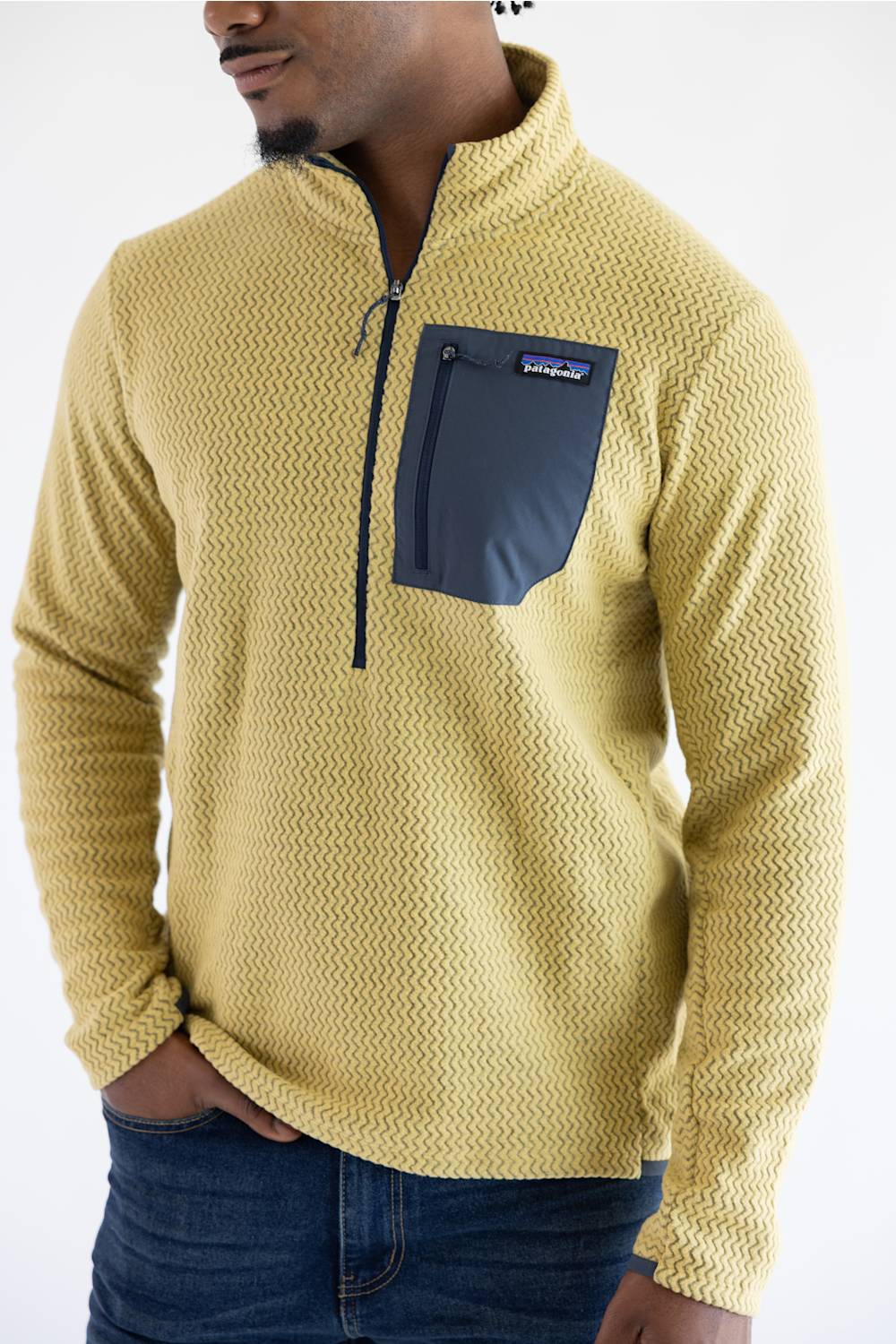 A man wearing a yellow textured quarter-zip fleece pullover with a dark navy chest pocket and zipper, paired with blue jeans, against a plain white background.