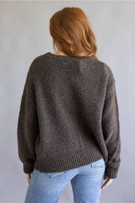 A woman with red hair is shown from behind wearing a dark brown fuzzy knit sweater and light blue jeans against a plain gray background.