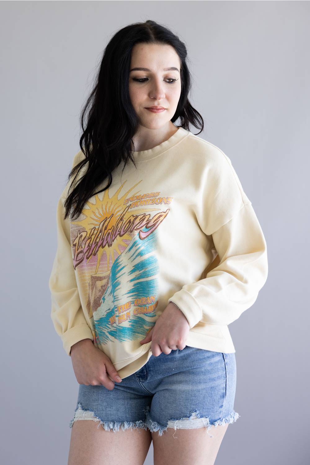 Woman wearing a light-colored sweatshirt with a graphic design on a plain background
