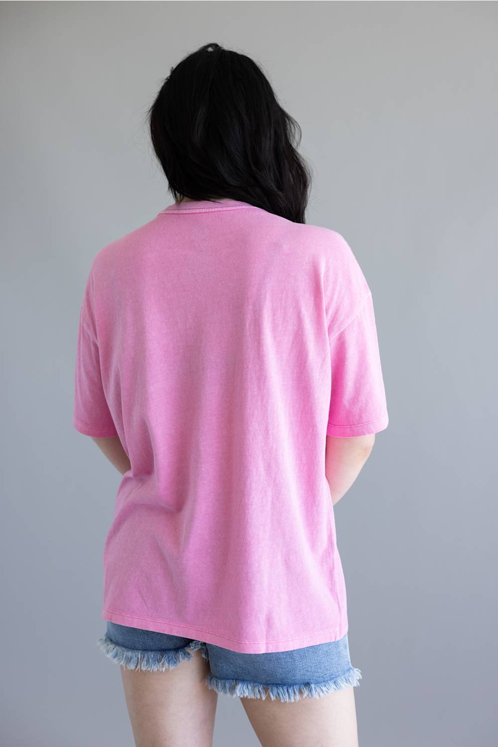 Person wearing a pink t-shirt and denim shorts against a plain background