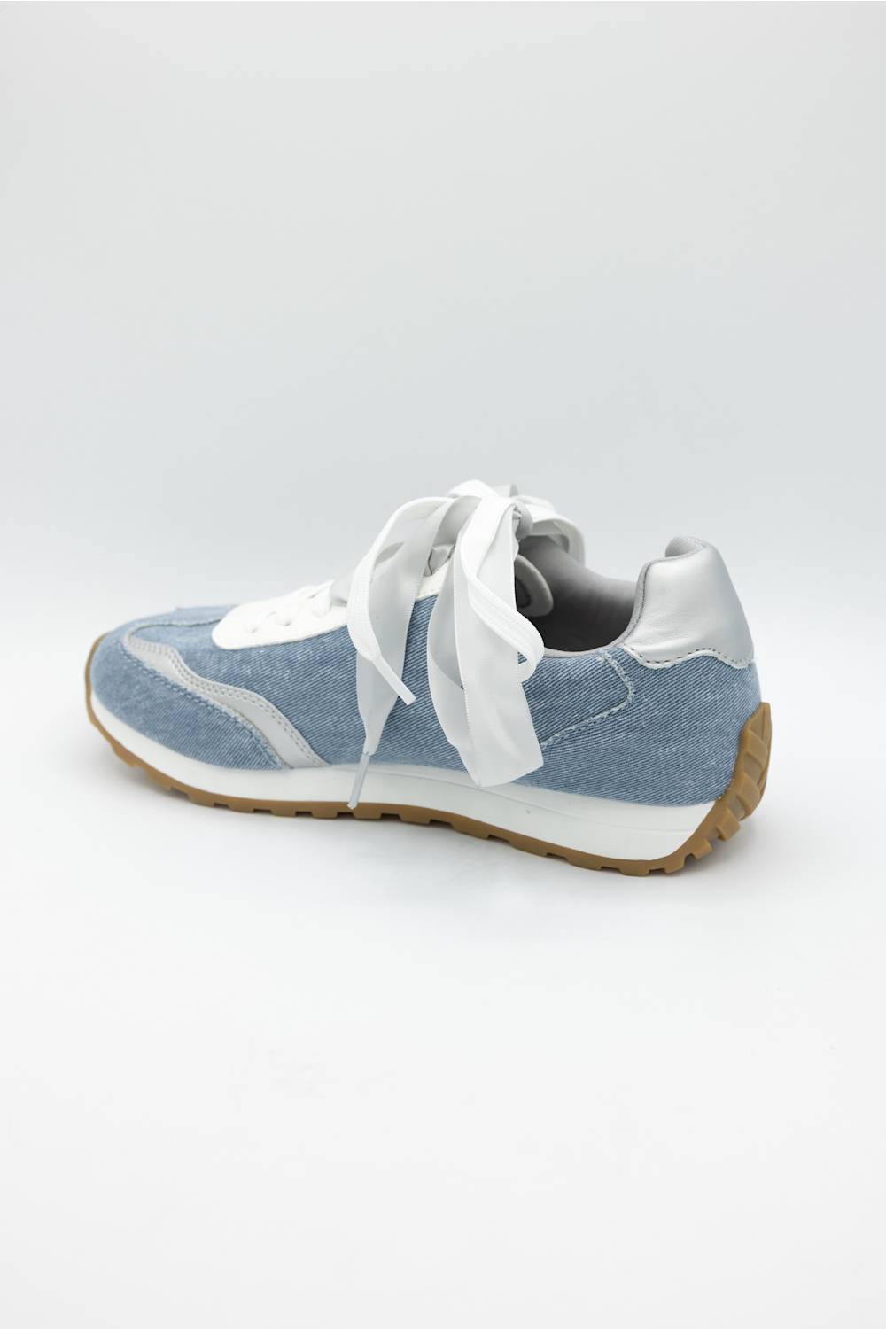 A light blue and white low-top sneaker with white laces and a brown gum sole, shown from a side angle on a light gray background.