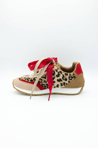 A low-top sneaker featuring a leopard print pattern on the side, beige suede-like panels, a red heel tab, and a red ribbon tied around the laces, shown against a plain white background.