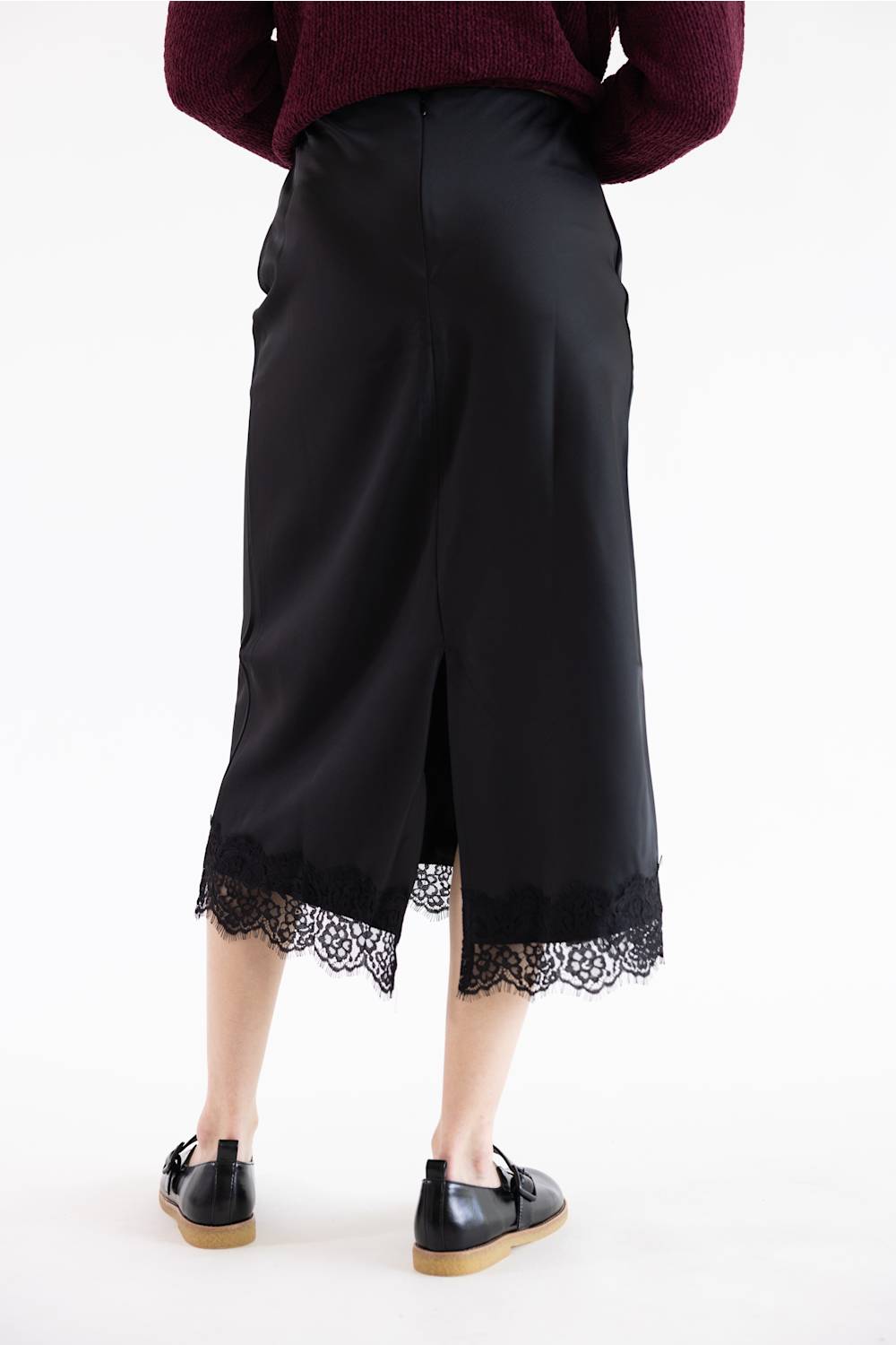 A person shown from the back wearing a black midi skirt with a lace hem, a burgundy sweater, and black shoes against a plain white studio background.