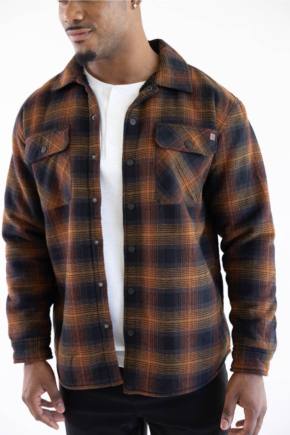A man wearing a dark brown and black plaid flannel shirt over a white t-shirt, photographed against a plain white background.