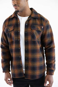 A man wearing a dark brown and black plaid flannel shirt over a white t-shirt, photographed against a plain white background.