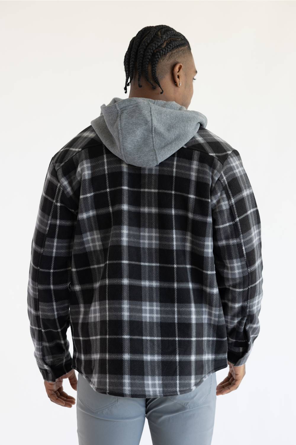 A person shown from the back wearing a black and gray plaid hooded flannel shirt over a light gray hoodie, paired with light blue jeans, against a plain white studio background.