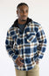 A man wearing a blue, brown, and beige plaid hooded flannel shirt over a dark gray t-shirt and khaki pants, standing against a plain white studio background.