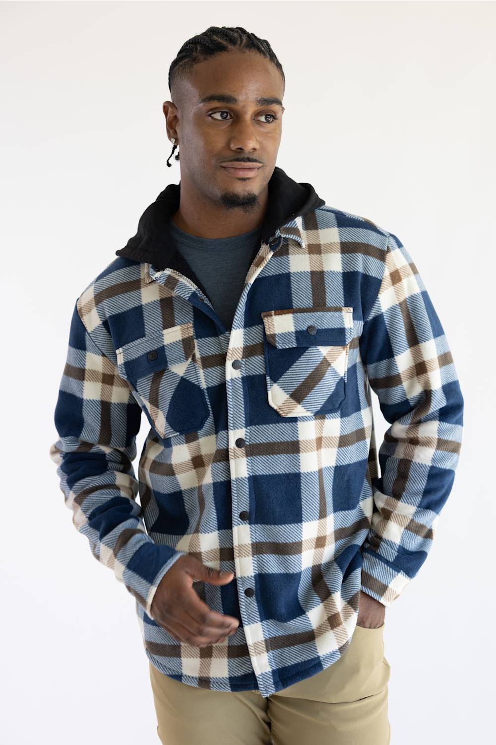 A man wearing a blue, brown, and beige plaid hooded flannel shirt over a dark gray t-shirt and khaki pants, standing against a plain white studio background.