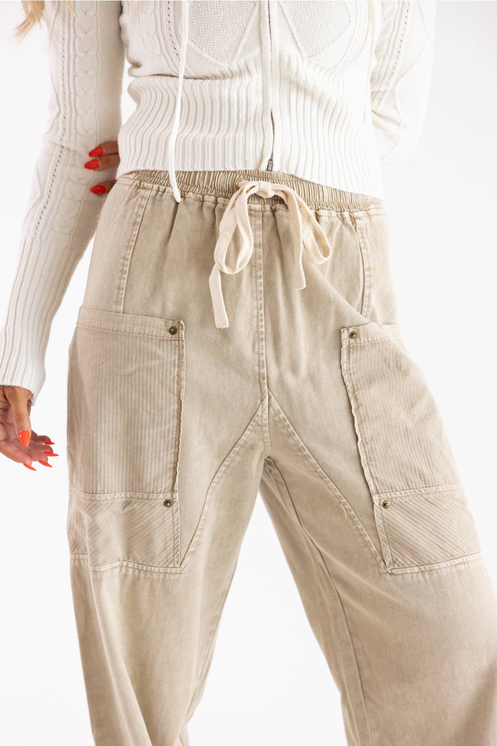 Beige corduroy cargo pants with a drawstring waist, worn by a model in a white ribbed sweater against a plain white background.