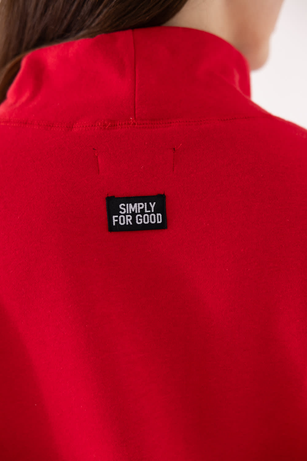 Close-up of the back of a bright red garment with a small black rectangular patch reading 'SIMPLY FOR GOOD' on the upper back.