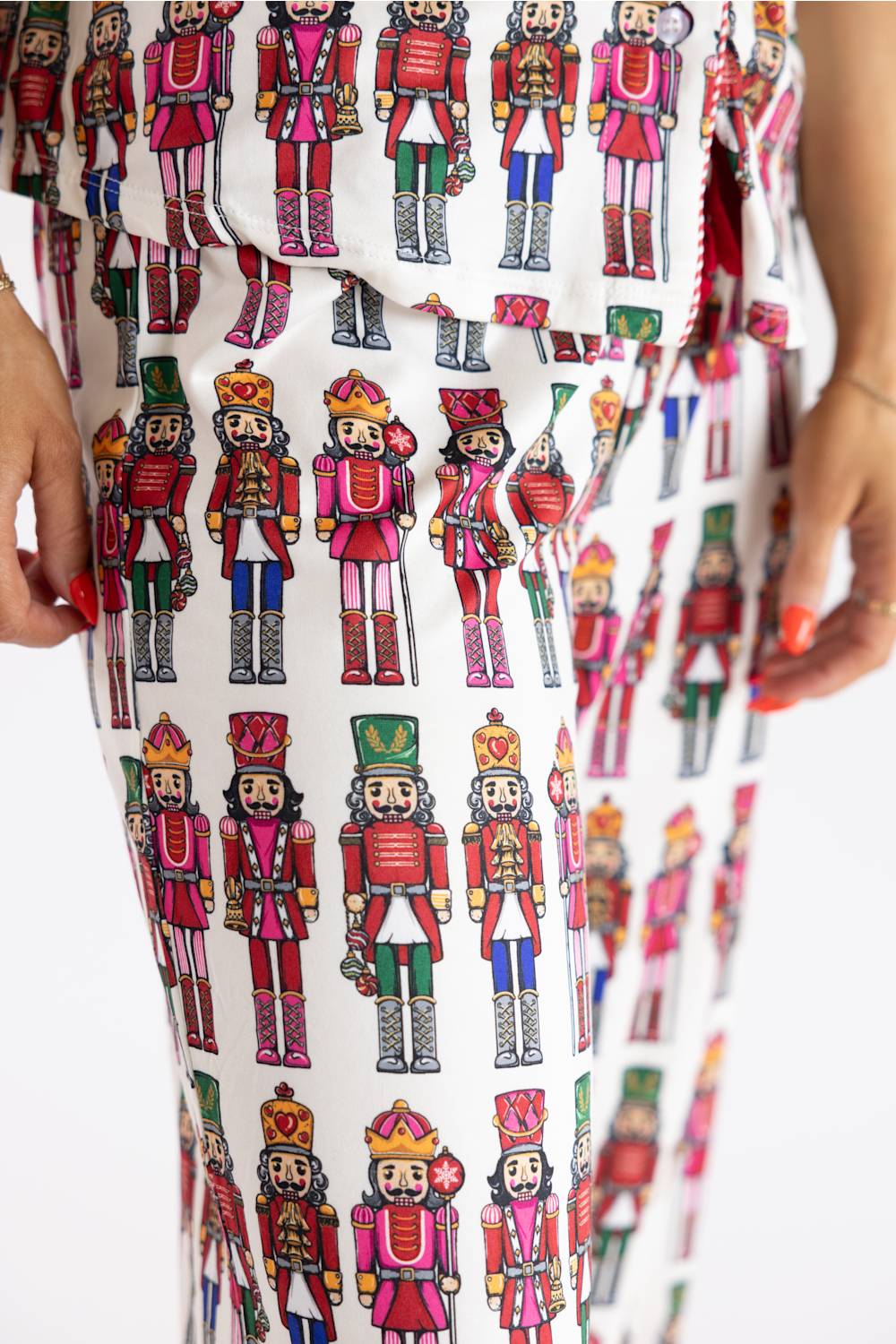 White pants featuring an all-over colorful nutcracker soldier pattern, shown on a model with hands visible at the sides.