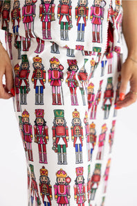 White pants featuring an all-over colorful nutcracker soldier pattern, shown on a model with hands visible at the sides.