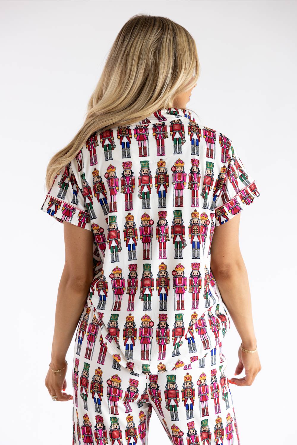 A woman shown from the back wearing a matching short-sleeve top and pants set with an all-over nutcracker print on a white background.