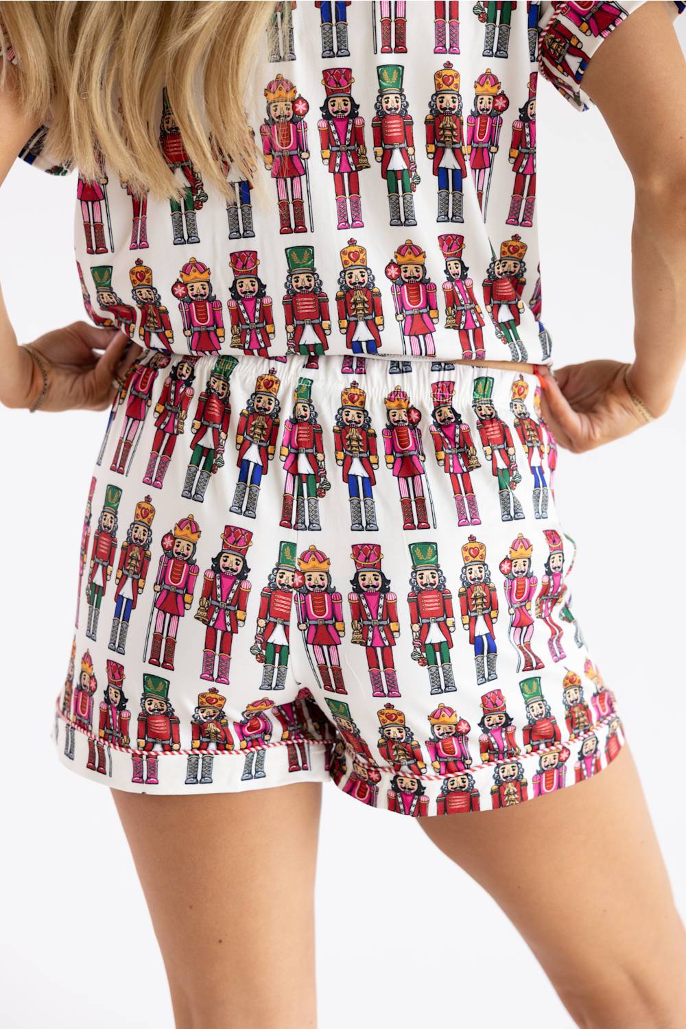 A woman wearing a white romper with an all-over colorful nutcracker soldier print, shown from the shoulders to mid-thigh against a plain white studio background.