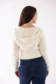 A woman shown from the back wearing a cream ribbed knit cropped hoodie sweater and dark blue jeans against a plain white background.