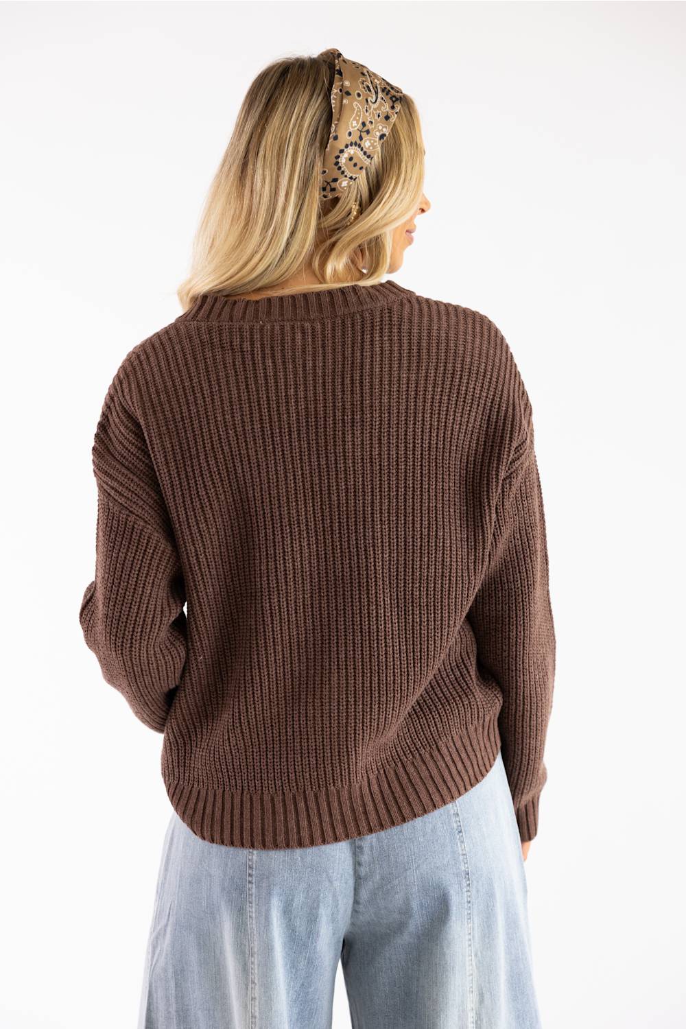 Back view of a woman with blonde hair wearing a patterned headband, a dark brown long-sleeve knit sweater, and light-wash jeans.