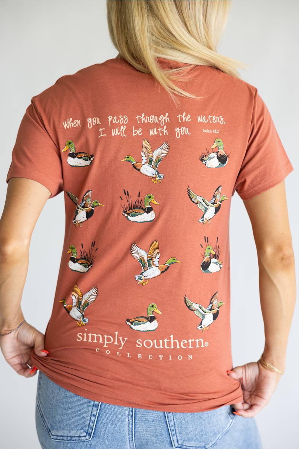 A terracotta-colored short-sleeve t-shirt shown from the back, featuring a graphic print of multiple flying mallards with handwritten-style text above and below. The brand 'simply southern.