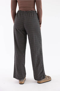 A person shown from the back wearing black and white horizontally striped wide-leg pants, a brown top, and tan slip-on shoes against a plain white studio background.