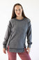 A woman modeling a dark gray mineral-wash long-sleeve sweatshirt with unique shoulder and hem details, paired with dusty rose pants, against a plain white background.