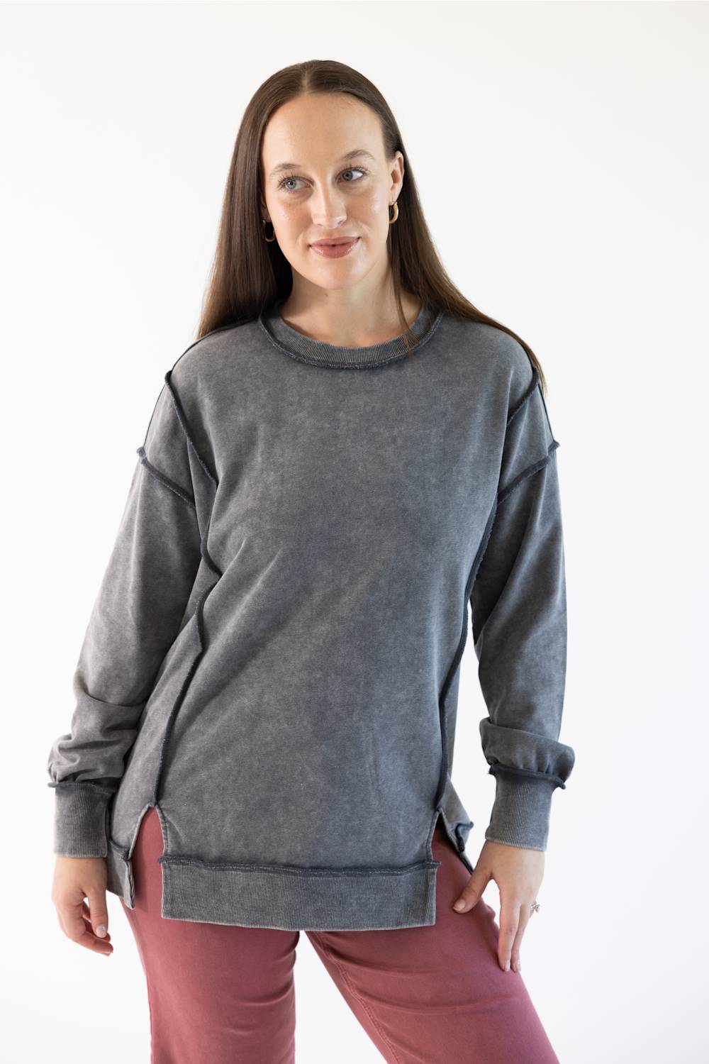 A woman modeling a dark gray mineral-wash long-sleeve sweatshirt with unique shoulder and hem details, paired with dusty rose pants, against a plain white background.