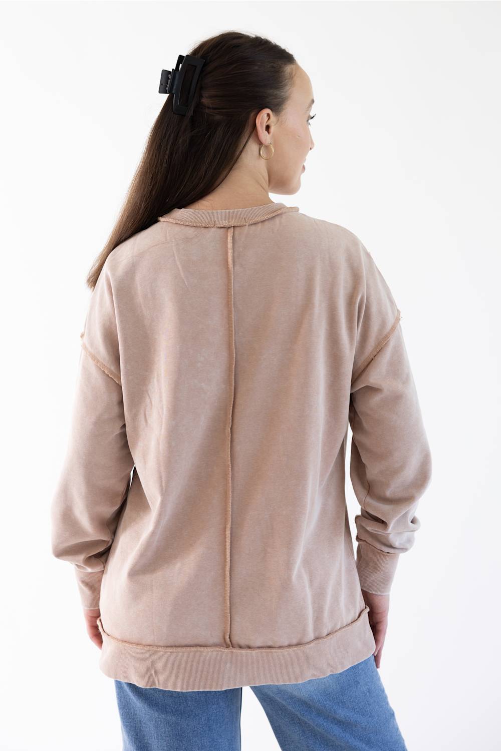 A woman shown from the back wearing a light beige long-sleeve sweatshirt and blue jeans against a plain white background.