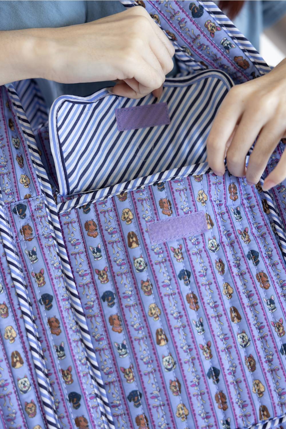 Close-up of a quilted apron with a purple and blue striped pattern featuring small dog illustrations, being held open by a person's hands to show the striped fabric lining.