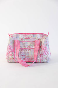A quilted fabric duffel bag with a floral patchwork pattern in pink, white, and blue, featuring pink gingham handles and a pink zipper, set against a plain white background.