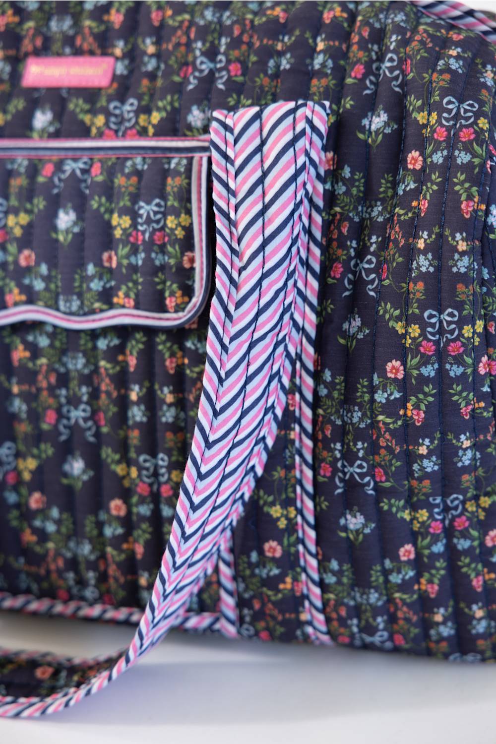 Close-up of a quilted fabric bag with a dark navy floral print and a pink, navy, and white striped strap, showing the texture and pattern details.