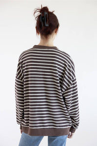 A woman viewed from the back wearing a brown and white striped sweatshirt with blue jeans on a white background
