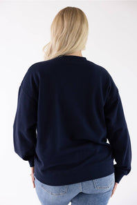Back view of a blonde woman wearing a navy blue Reflex fleece crewneck sweatshirt and blue jeans.