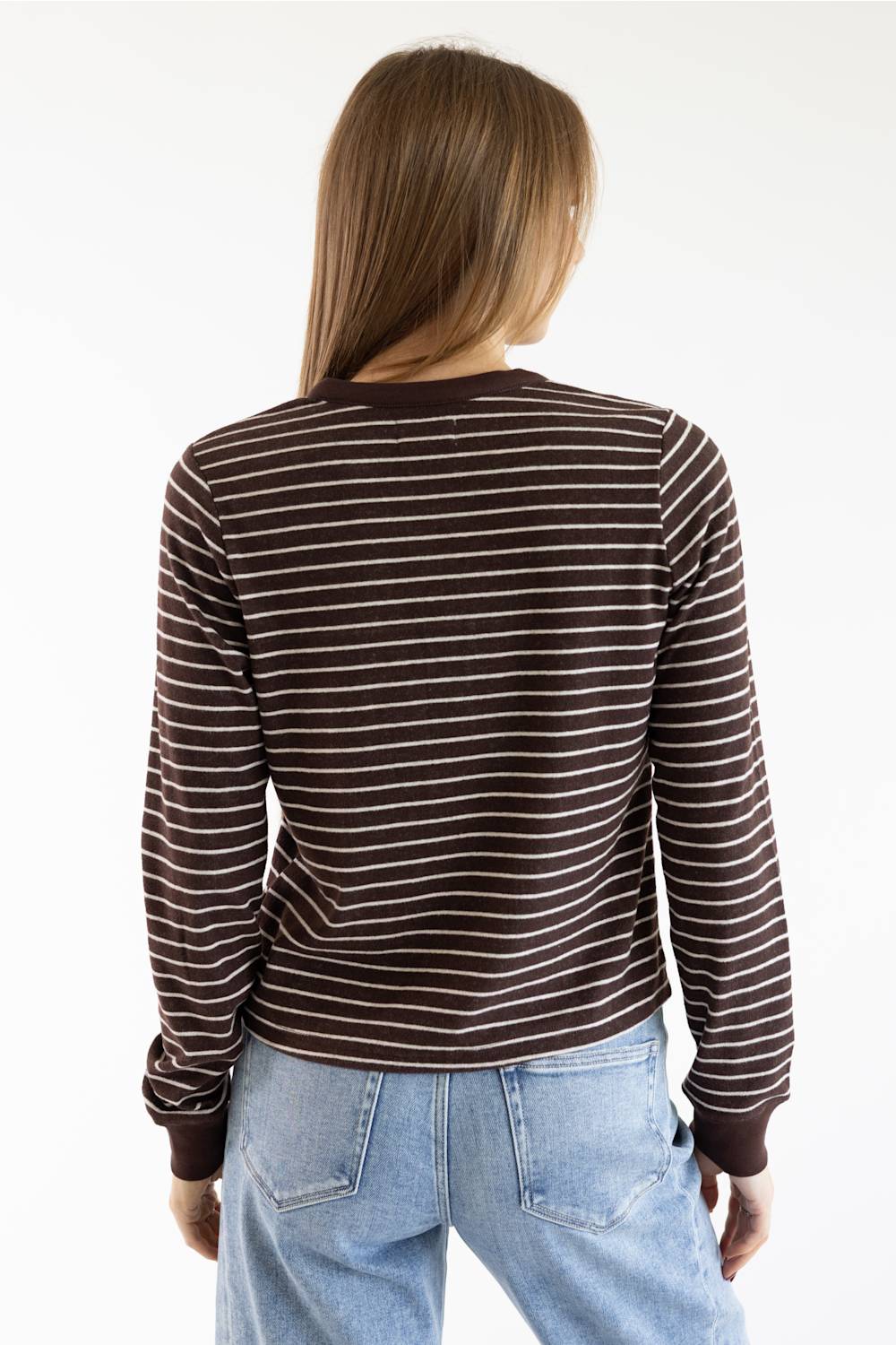 A woman viewed from behind wearing a brown and white striped long-sleeve shirt and light blue jeans against a plain white background.