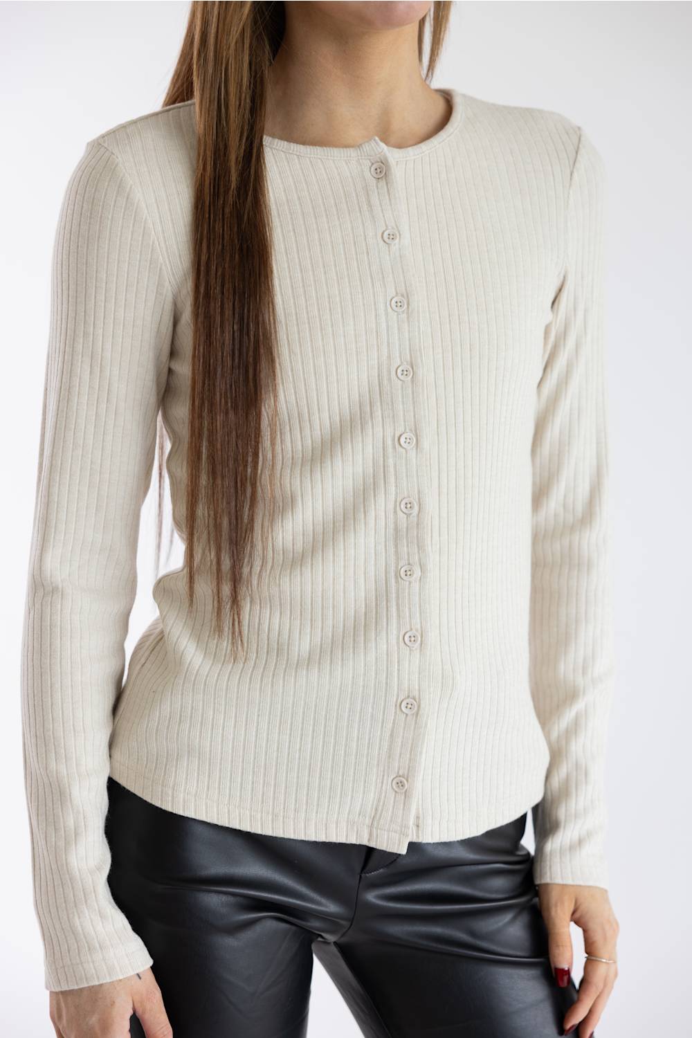 A woman wearing a ribbed cream-colored long-sleeve button-up cardigan sweater and black faux-leather pants, shown from the neck down against a plain white background.