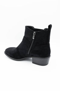A black suede ankle boot with a side zipper, low block heel, and pull tab, shown from a side profile on a white background.