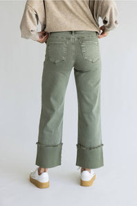 A person shown from the back wearing sage green wide-leg cropped jeans with rolled frayed hems, a beige sweater, and white platform sneakers against a light gray studio background.