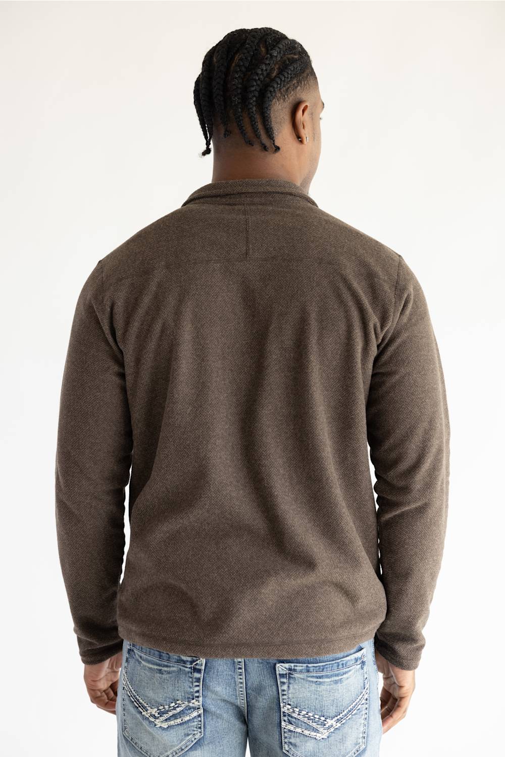 A man viewed from behind wearing a brown long-sleeve knit sweater and blue jeans against a plain white background.
