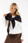 A blonde woman wearing a white knit sweater and a brown satin skirt, modeling a dark brown and navy plaid scarf tied around her neck against a plain white background.