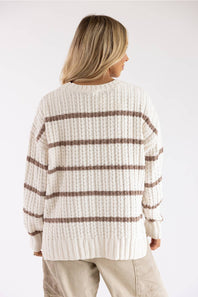 Back view of a model wearing a Paper Cut Clothing / Pink Rose white and tan striped crewneck tunic sweater paired with beige utility pants against a plain backdrop.
